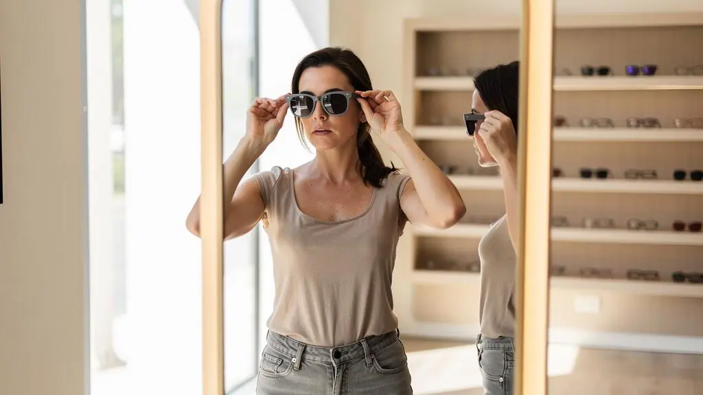 Une femme essaie des lunettes de soleil à monture bicolore devant un miroir